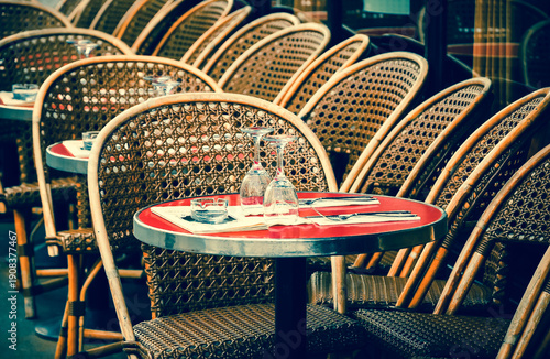 Parisian typical cafe terrace with round tables and wicker chairs set for lunch time. Paris, France. Retro blue red photo.