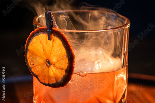 whiskey cocktail served on the rocks garnished with a dehydrated orange slice with dramatic lighting served on a wooden surface.