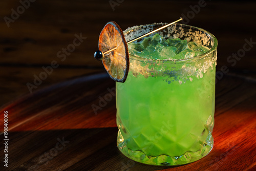 Bright Green Margarita on the rocks with salt and a dehydrated lime wheel with dramatic lighting