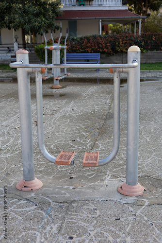 Outdoor fitness equipment installed in a public park. Metal gym machines with plastic elements designed for open-air workouts.
