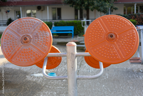 Close-up of an outdoor fitness machine with round rotating platforms for core training and balance exercises. Visible texture of plastic surfaces and metal structure.
