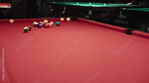 Fast break shot scatters racked billiards balls across red table, white cue ball slams triangle causing colorful pieces to fly, dynamic hit by cue captures nightlife energy during match in club