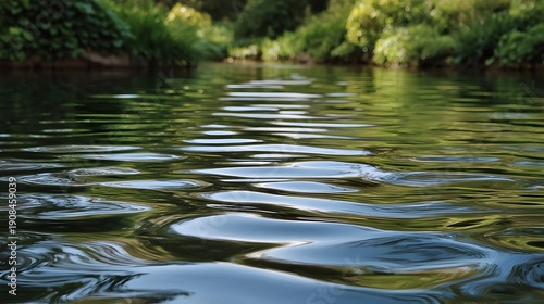 Gentle water ripples on a calm river s surface reflect lush green foliage and trees in soft daylight