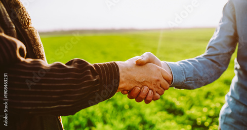 Two people shake hands in a green field during the day. This scene captures a moment of agreement or friendly greeting in nature. Concept for agriculture and business.