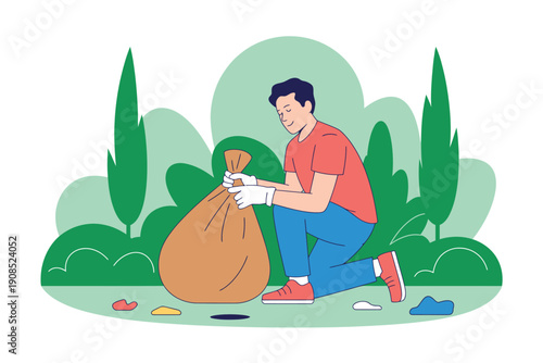A man in a red shirt and blue jeans kneeling down to pick up trash and put it in a large brown bag.