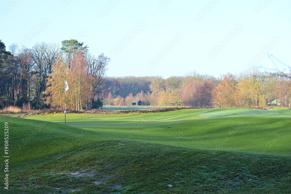 Obraz premium A wide view of the rolling green hills and fairways of a golf course surrounded by autumn trees in the countryside between Vught and 's-Hertogenbosch, Netherlands.