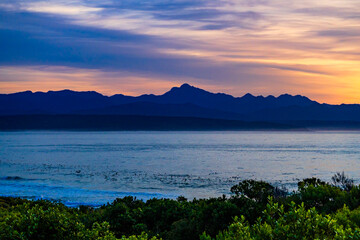 Vibrant sunrise over the ocean with mountain silhouettes in South Africa, Plettenburg bay.