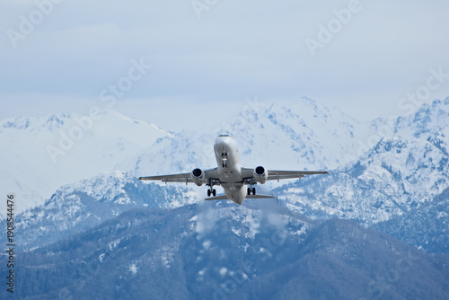 Tableau sur toile White Airplane Taking Off Against Snowy Mountains in Cloudy Weather