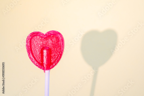 Heart-shaped lollipop standing on a plain background, casting a distinct shadow