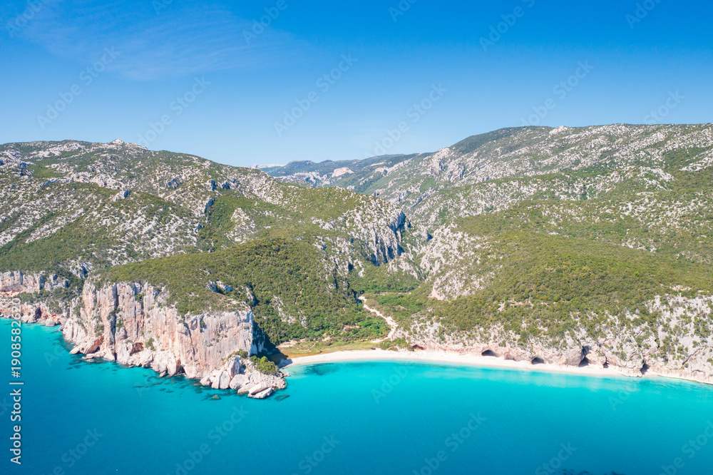 Obraz premium Aerial view of Cala Luna beach on the coast of Baunei and Dorgali, Sardinia, Italy. Turquoise water, white sandy shoreline and dramatic limestone cliffs along the Gulf of Orosei.
