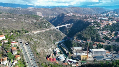 Aerial view of Rijeka, Croatia, showcasing its dramatic river canyon, historic Trsat Castle, and modern infrastructure under a partly cloudy sky.