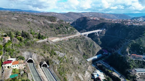 Aerial view of Rijeka, Croatia, showcasing its dramatic river canyon, historic Trsat Castle, and modern infrastructure under a partly cloudy sky.
