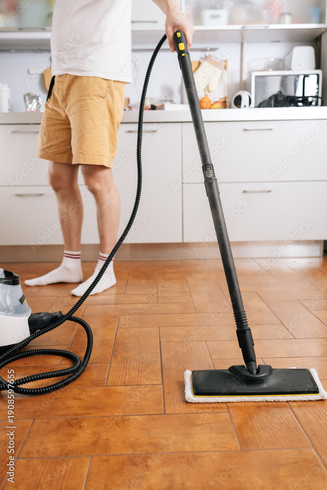 Fototapeta premium Person using steam cleaner device to sanitize and deep clean kitchen floor, performing domestic chore for efficient home sanitation and hygiene. Concept of maintenance modern home appliance.
