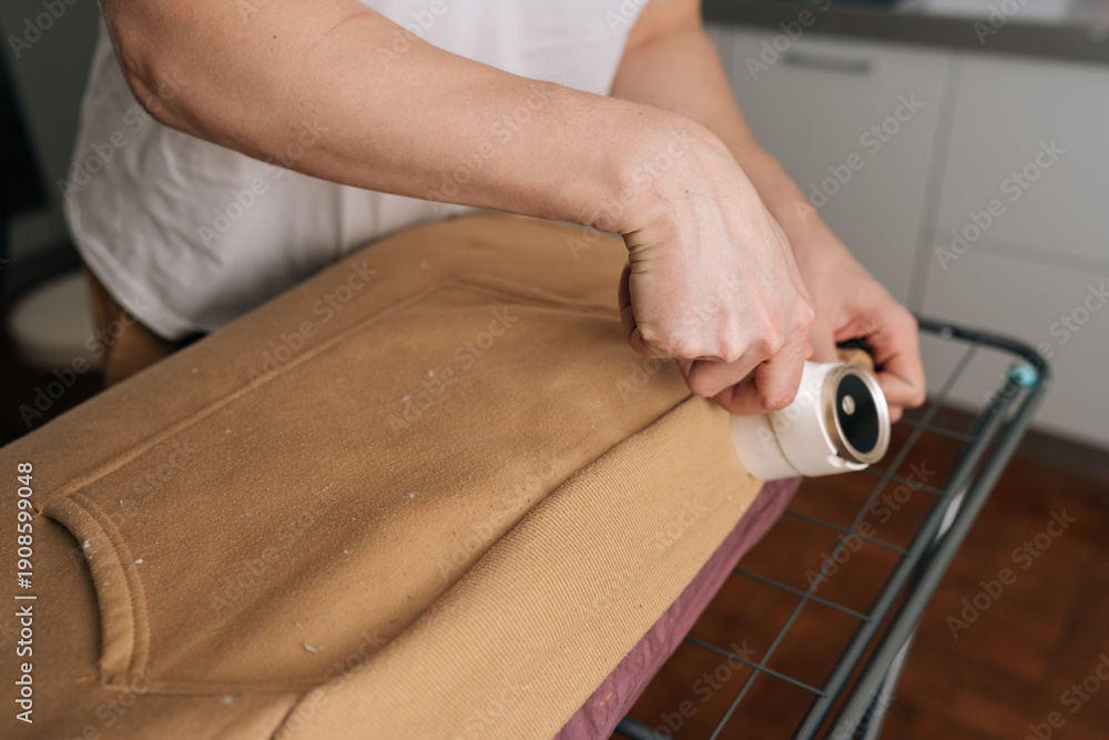 Obraz premium Male hands using battery lint remover on brown sweater, shaving away fuzz and pilling to restore smooth texture and refresh worn knitwear for everyday clothing care. Concept of effective fabric care.
