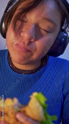 Young woman wearing headphones eats a hamburger