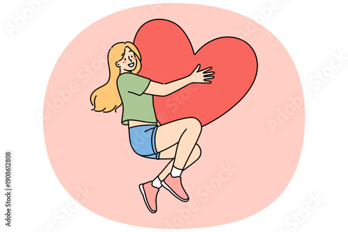 Happy teenage girl hugs large heart-shaped valentine card, rejoicing at coming of february holiday. Woman in love feels euphoria and romantic mood after receiving valentine day gift