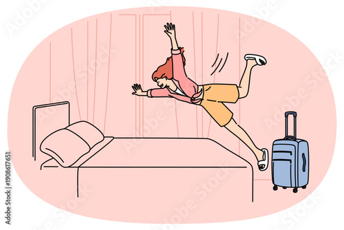 Happy woman tourist jumps on hotel bed, rejoicing at onset of vacation and opportunity to visit sunny resort. Girl with travel suitcase is in hotel and happily plops down on bunk to relax