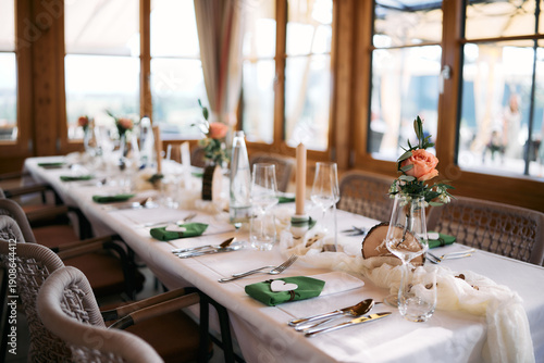 Valokuva Tastefully decorated wedding reception table with floral centerpieces, candles, glassware, and place settings in a bright restaurant interior, prepared for guests