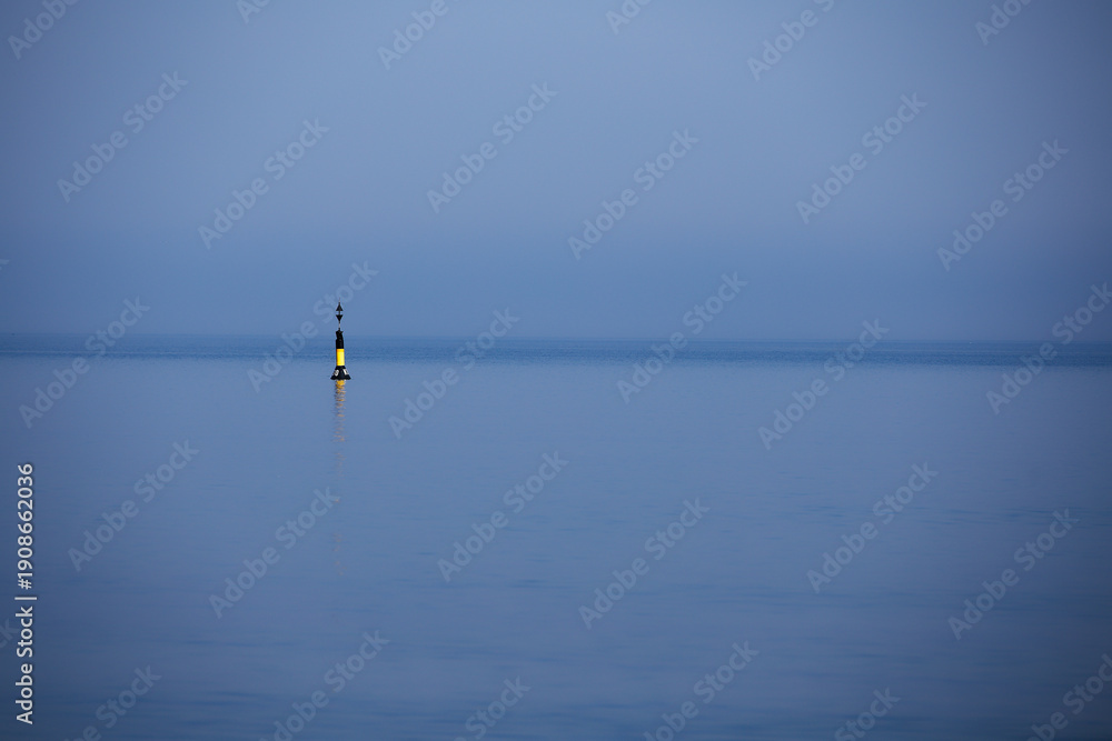 Fototapeta premium Lone navigation buoy in calm blue sea under hazy sky