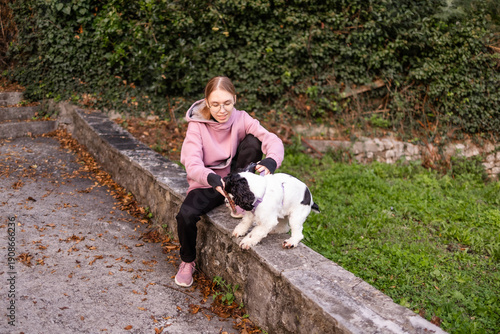 Teenage blonde Slavic girl sitting on a stone wall and petting her Russian spaniel dog in Montenegro