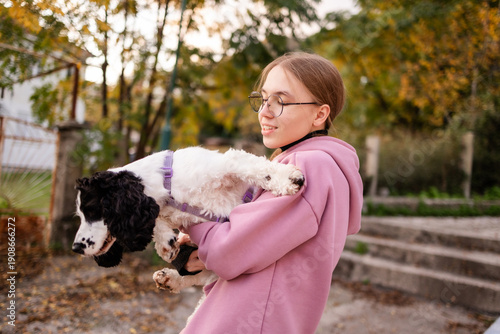 Teenage blonde Slavic girl carrying her Russian spaniel dog along a stone wall in Montenegro