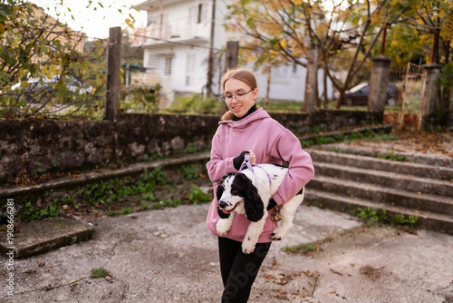 Teenage blonde Slavic girl carrying her Russian spaniel dog along a stone wall in Montenegro