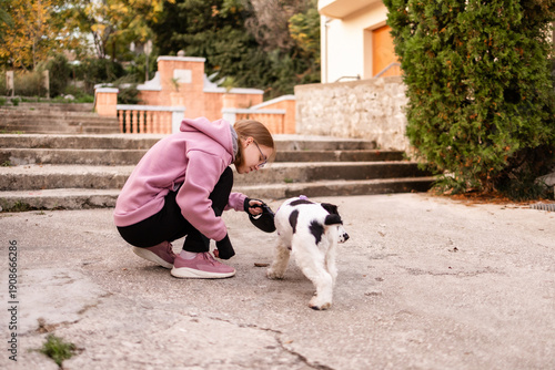 Teenage blonde Slavic girl pulling the leash of a resisting Russian spaniel dog on a concrete path in Montenegro