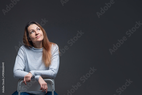 Foto Woman sits on chair and looks up with calm expression in studio setting during i