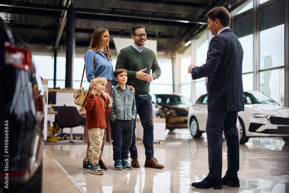 Obraz premium Happy parents with kids communicating with car salesperson in showroom.