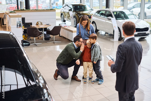 Happy family having fun while buying new car in showroom.