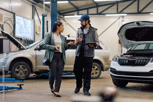 Mid adult woman talking to mechanic about her car problems in repair shop.