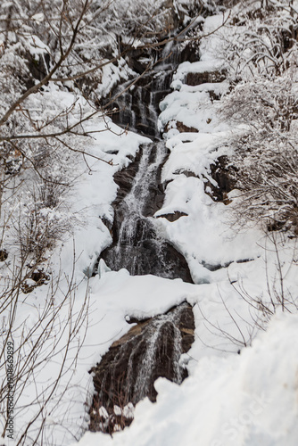Winter waterfall cascading through snow-covered rocks, capturing cold-season nature, flowing water, frozen textures, and the quiet beauty of a mountain landscape
