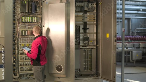Electrical engineer inspecting industrial control cabinet and circuit breakers at factory