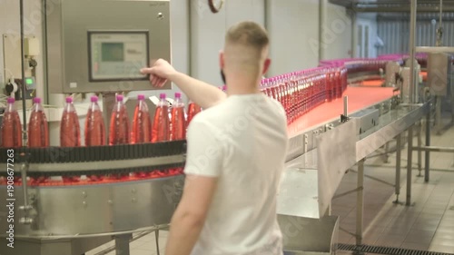 Factory worker operating touch screen control panel on automated bottling production line.