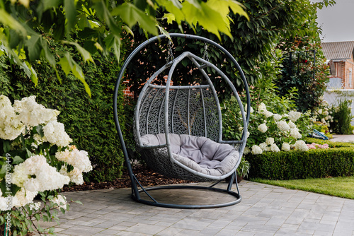 Hanging egg chair on patio in lush garden with hydrangea blooms