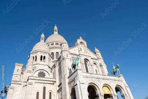 Low angle view of the white domes and intricate stone architecture of the Sacre Coeur Basilica in Montmartre, Paris, under a clear blue sky, famous French religious landmark and tourist attraction