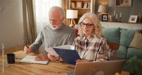 Photos An older couple is sitting at a wooden table in their living room