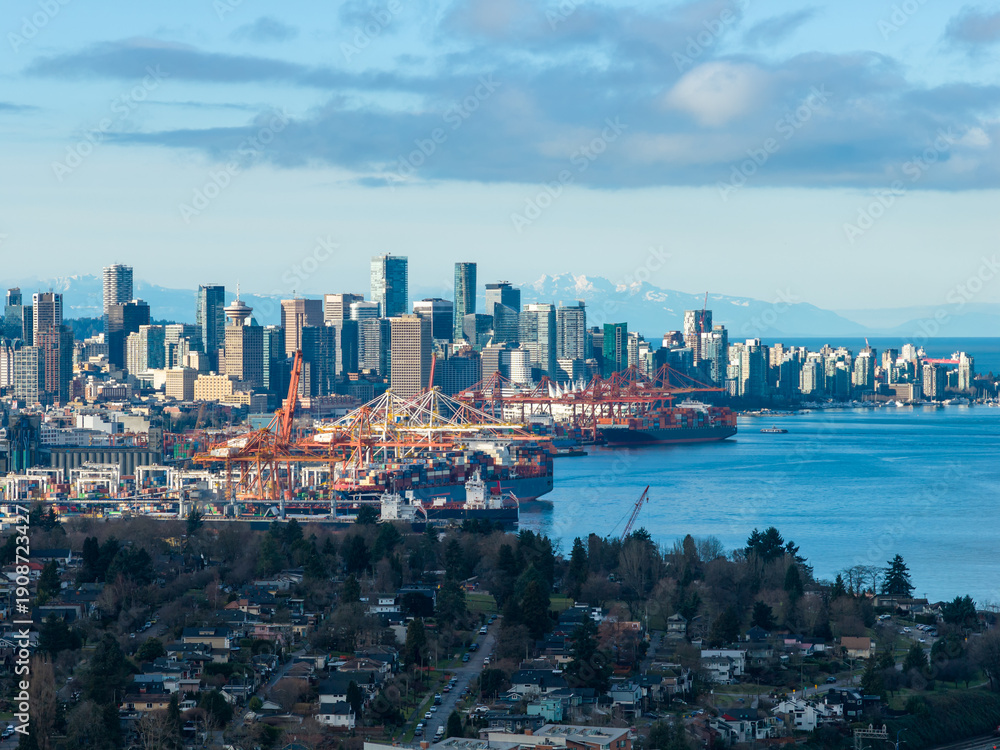 Naklejka premium Vancouver Skyline With Port Cranes Over Water and Mountain Backdrop, A Coastal Cityscape
