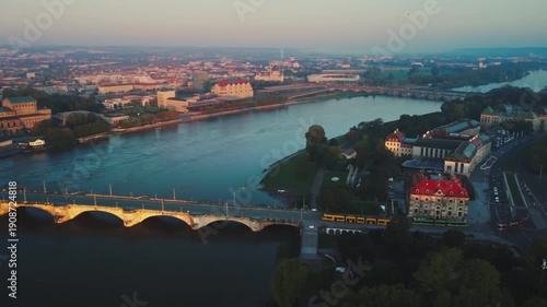 At dawn, aerial footage pulls back from a tram traveling across the Augustus Bridge, revealing the bridge and Dresden's Old Town.