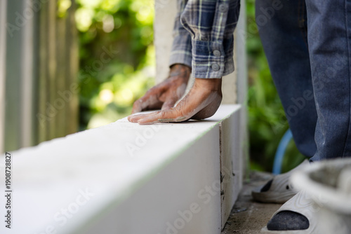 Worker aligning aerated concrete block during wall construction