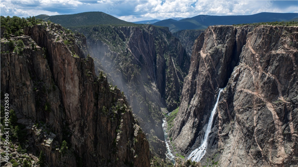 Obraz premium Powerful Waterfall Plunging into Misty Rock Canyon Below