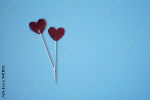 Two red heart-shaped lollipops are placed on a solid light blue background for the February 14 celebration. Concept: Concept of February 14 romantic love.