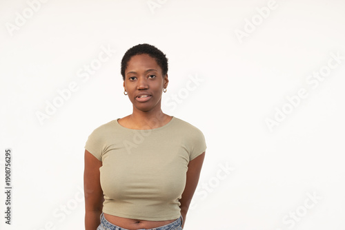 Portrait of young woman with short Afro hair standing against white background. Lady in casual clothes showing blank expression in white studio