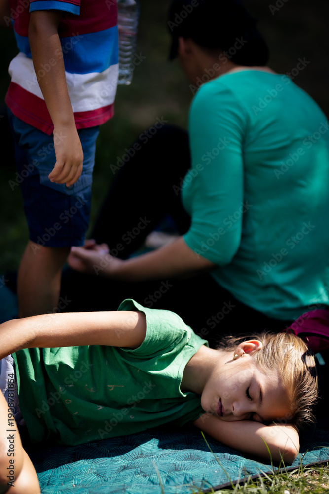 Fototapeta premium Young girl sleeping outdoors on a blanket during a family gathering under the sun