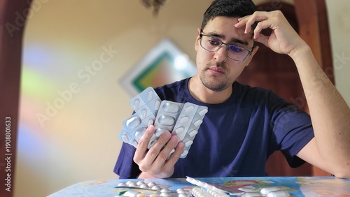 Fotografía Man looking stressed holding multiple blister packs of medication, contemplating