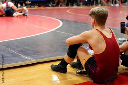 Young Man, a High School Wreslter is Sitting Nest to the Mat at a Wresting Tournament