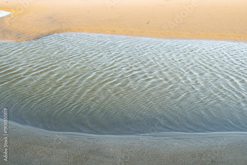 wind create ripples on the water surface, a tiny puddle of fresh water trapped on the sand after a torrential rain storm