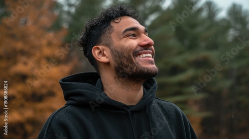 mixed race man front facing with plain black hoodie, mock up style, with fall forest smiling

