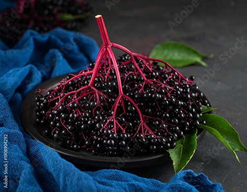 Dark berries on dark plate with blue cloth, vibrant red stems