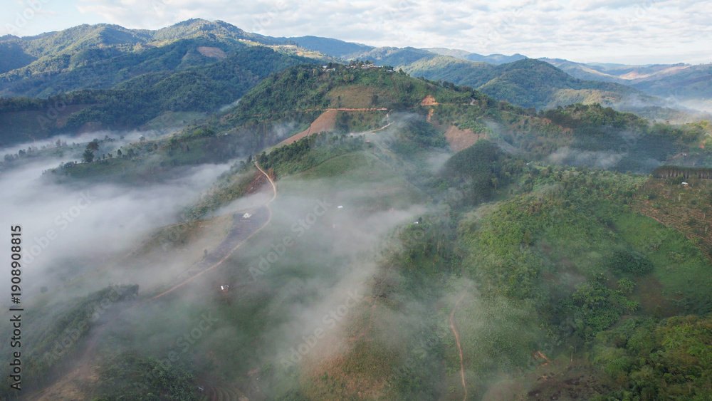 Fototapeta premium Aerial view of the rural village and dirt road in the mountains on foggy morning by drone